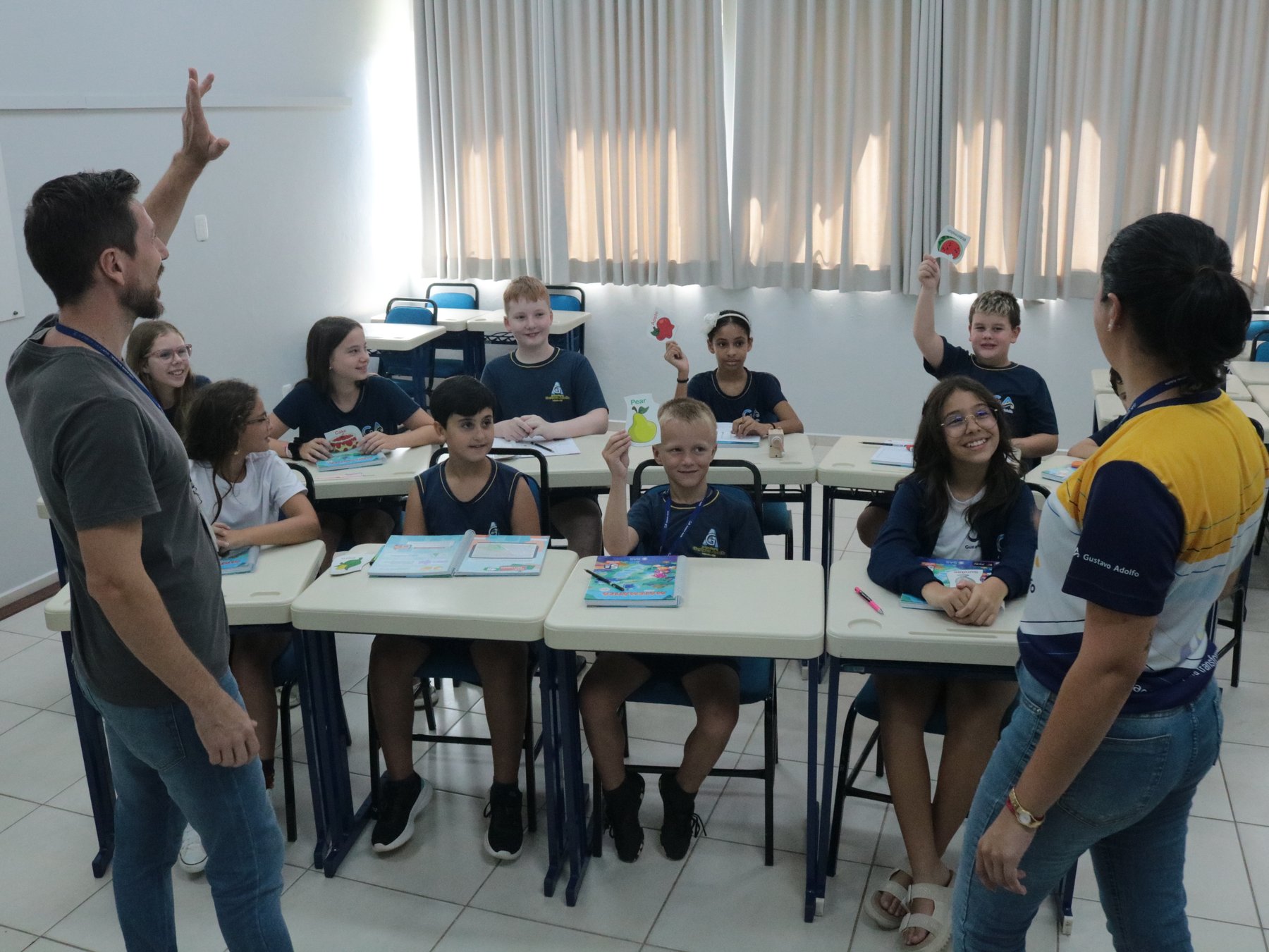 Professor do GA conduzindo atividade em sala de aula, estudantes reunidos em grupos