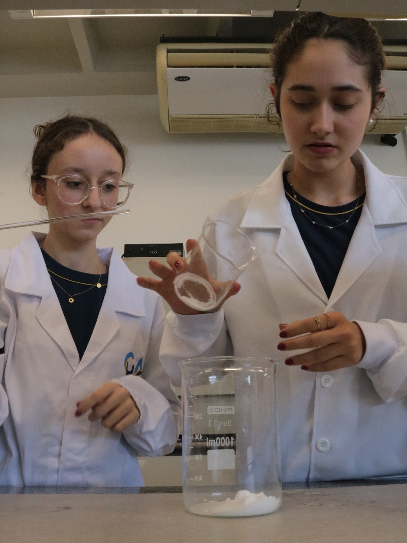 Dois estudantes do GA de jaleco durante prática no laboratório